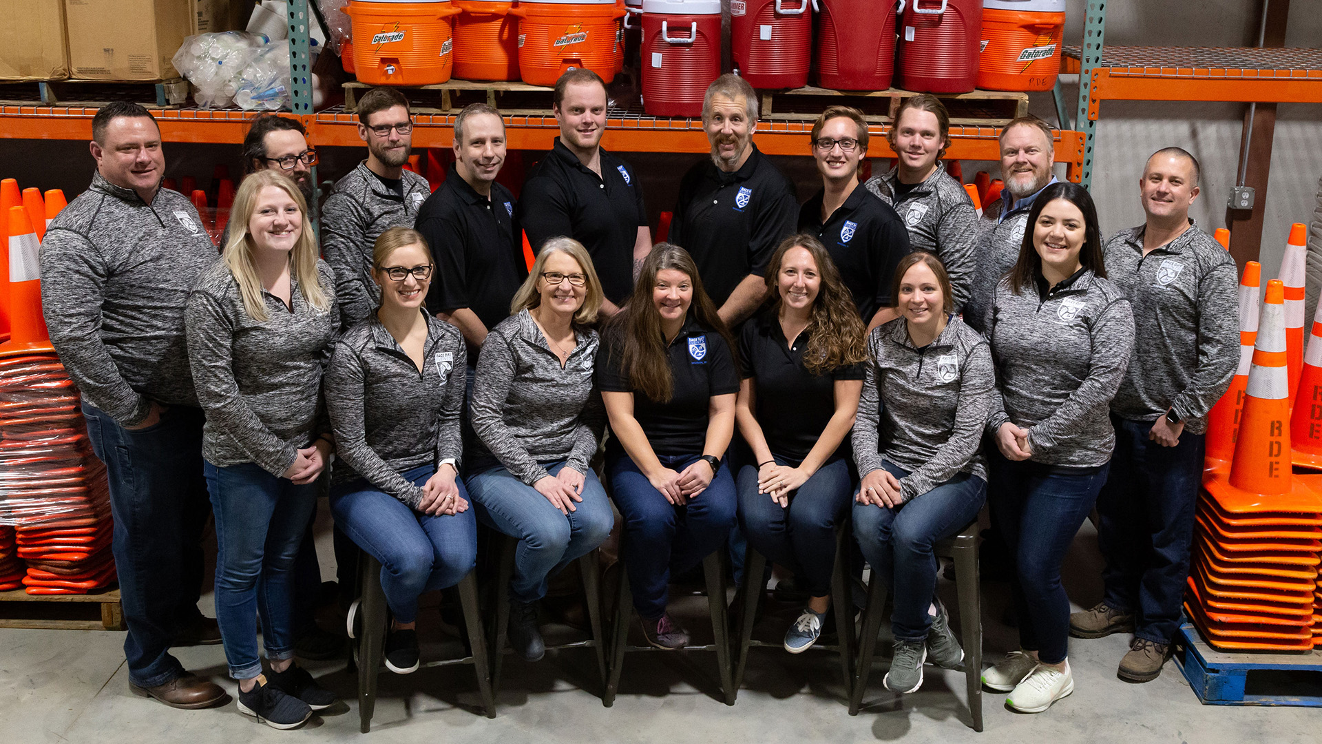 Race Day Events' staff photo; their team standing in front of race equipment like traffic cones and gatorade coolers.