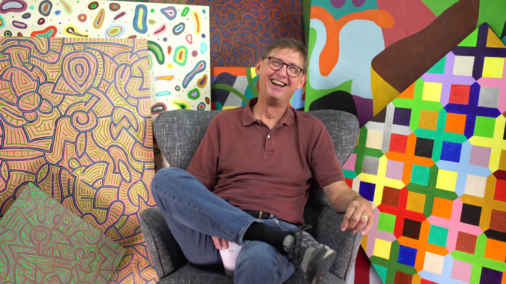 Earl Sherman sits in a chair among his art and laughs.