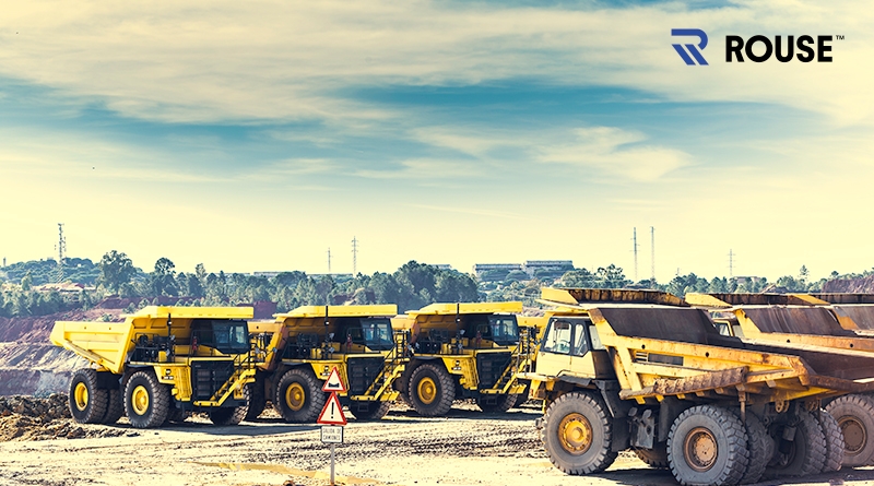 Dump trucks on a rental lot with a blue sky in the background and the Rouse logo in the top right.