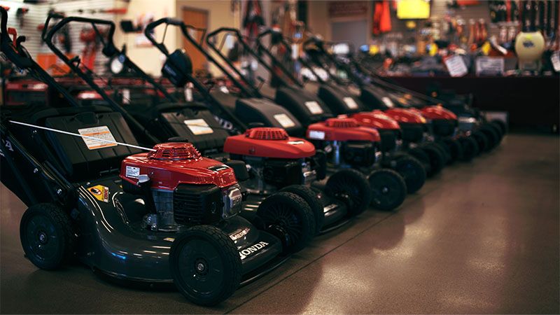 A row of lawnmowers sits as inventory within a rental store.
