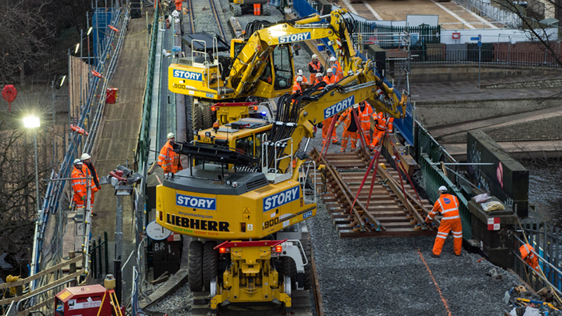 Story plant equipment works on a rail line with Story contracting employees helping assemble the rail line.