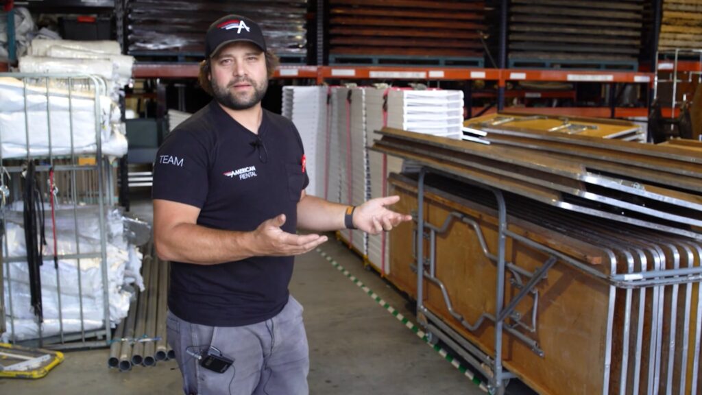 Brad Kniep in the American Rental warehouse stands next to a stack of tables that are pre-staged to go on the next truck.